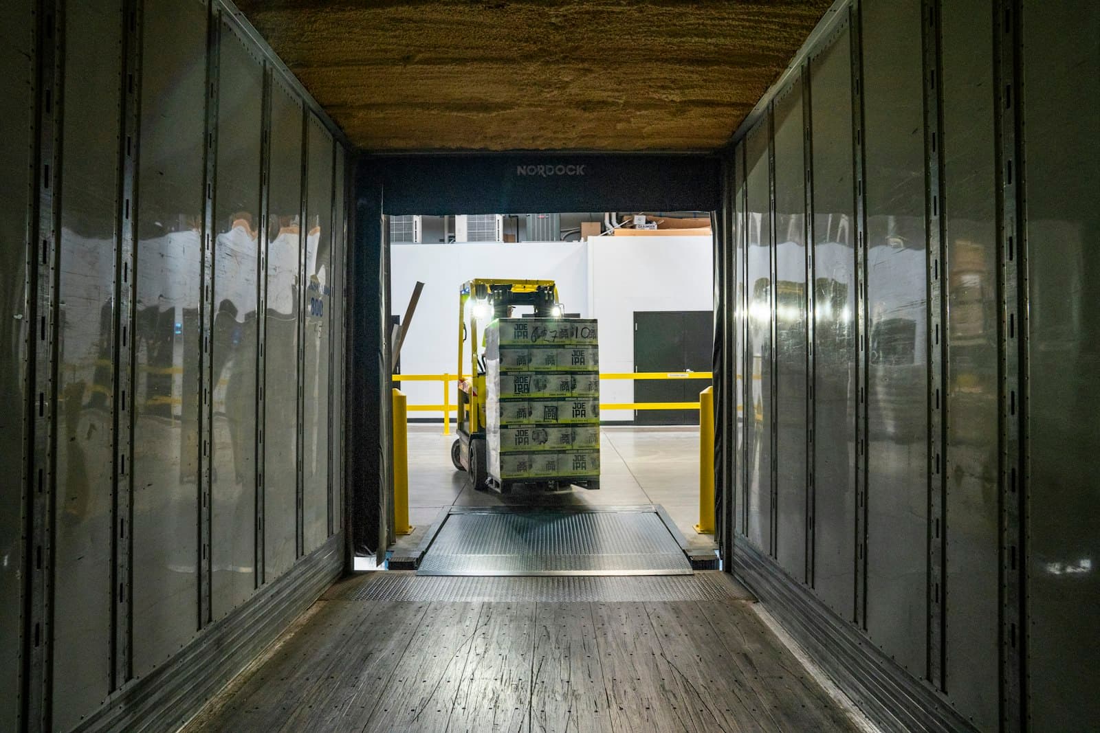 A forklift loading a shrink-wrapped pallet of goods into a truck trailer at a warehouse loading dock